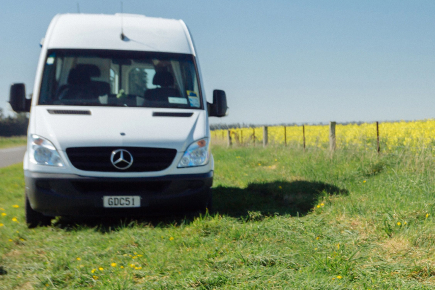 Motorhome on grass with yellow flowers in field next door.