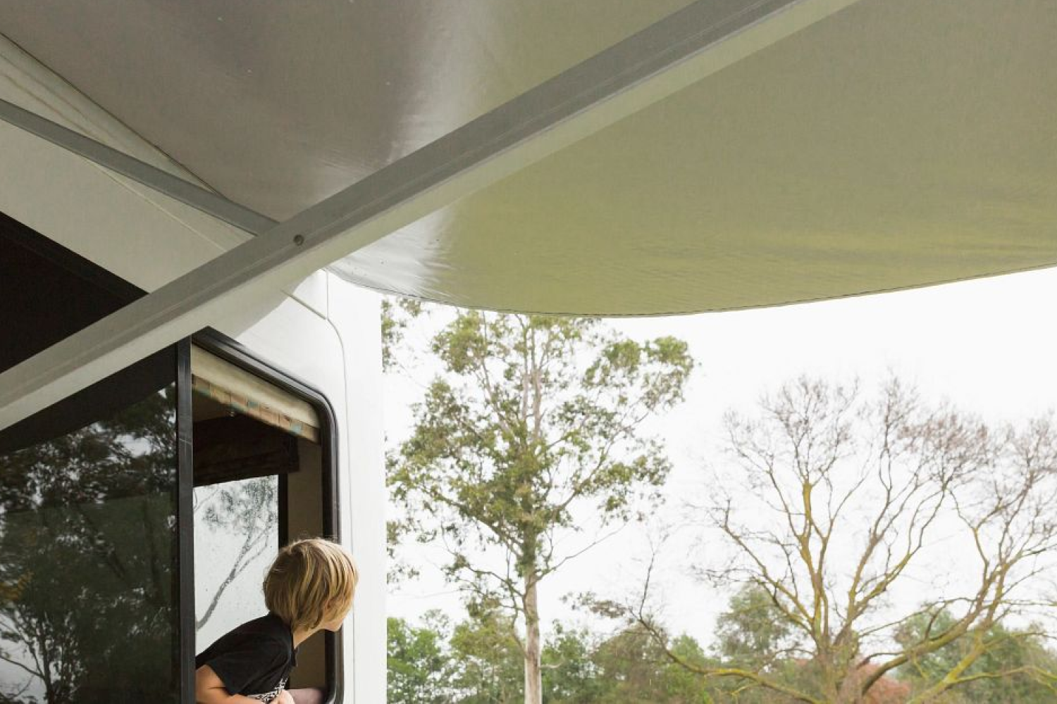 awning on motorhome with boy looking out window at it