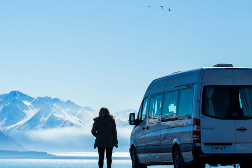person standing next to motorhome with snowy mountains