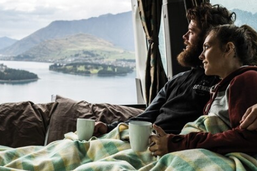 couple cosy in lounge of motorhome parked up enjoying some green mountains scenery outside their window